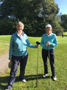 two ladies in turquise jumpers holding golf clubs